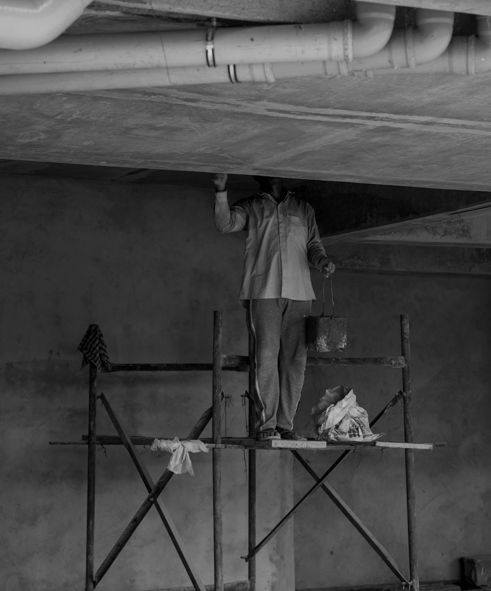 grayscale photo of man standing on ladder