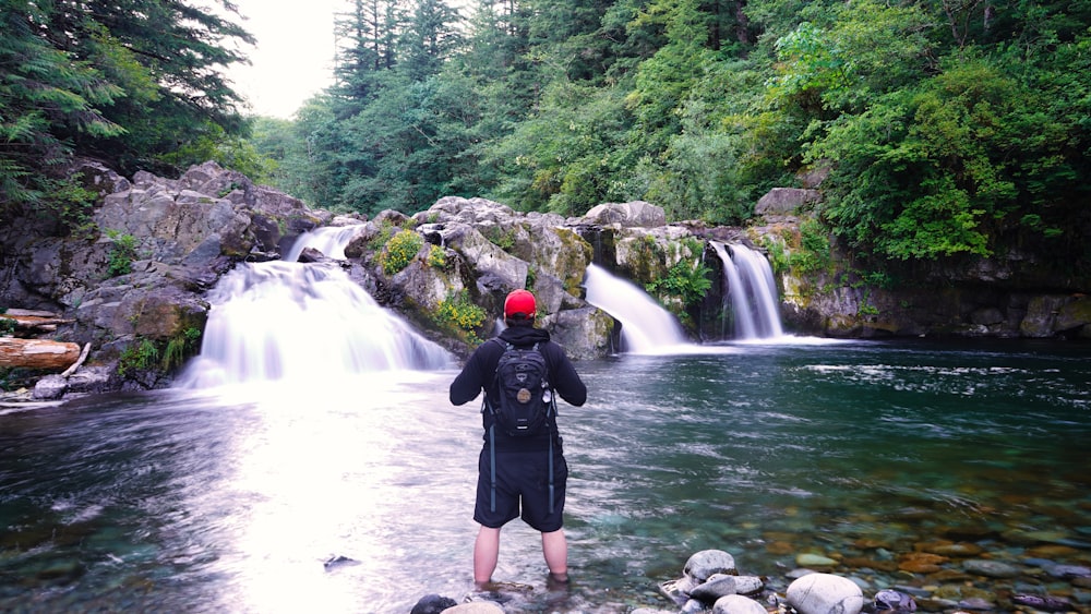 person in black jacket and black shorts standing on rock in front of waterfalls during daytime