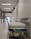 A hospital hallway is depicted with a gurney positioned in the foreground. The corridor is clean and well-lit, with signs indicating different departments such as 'GASTROENTEROLOGIE.' Several closed doors and white walls line the hallway, creating a sterile and orderly environment.