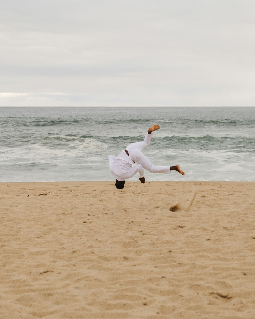 mulher na camisa branca de manga comprida e calças pretas que correm na costa da praia durante o dia