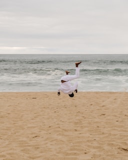 woman in white long sleeve shirt and white pants running on beach during daytime