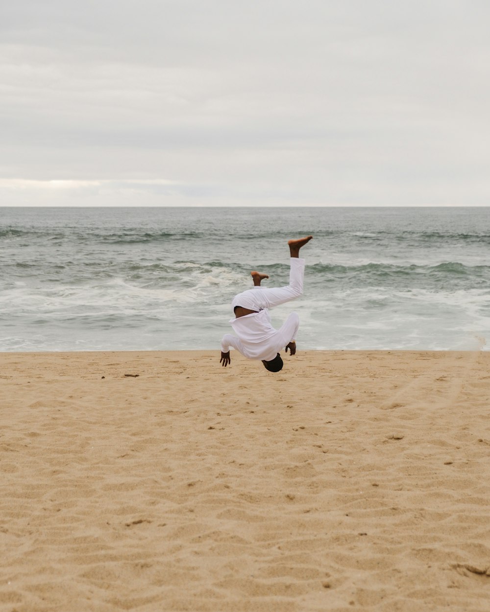 mulher na camisa branca da manga comprida e calças brancas que correm na praia durante o dia