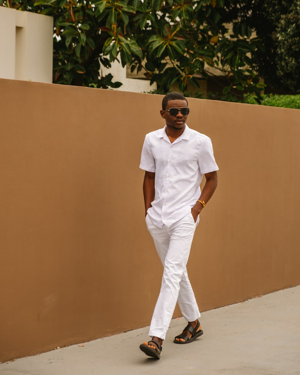 Foto hombre con camiseta blanca con cuello redondo y pantalón blanco parado  cerca de una pared marrón – Imagen Gafas hombre gratis en Unsplash