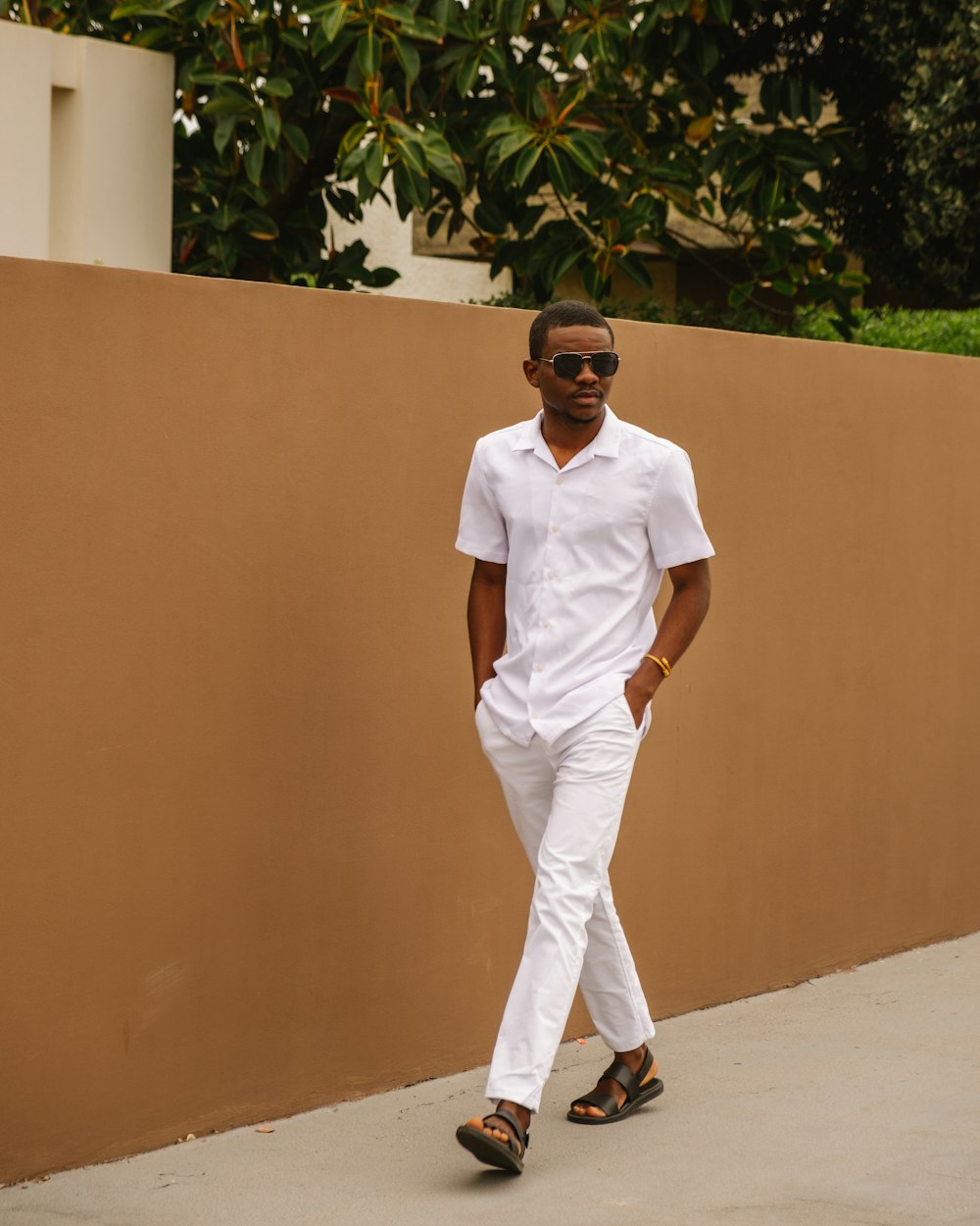 man in white crew neck t-shirt and white pants standing near brown wall