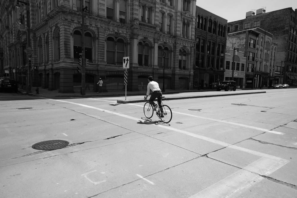 grayscale photo of man riding bicycle on road