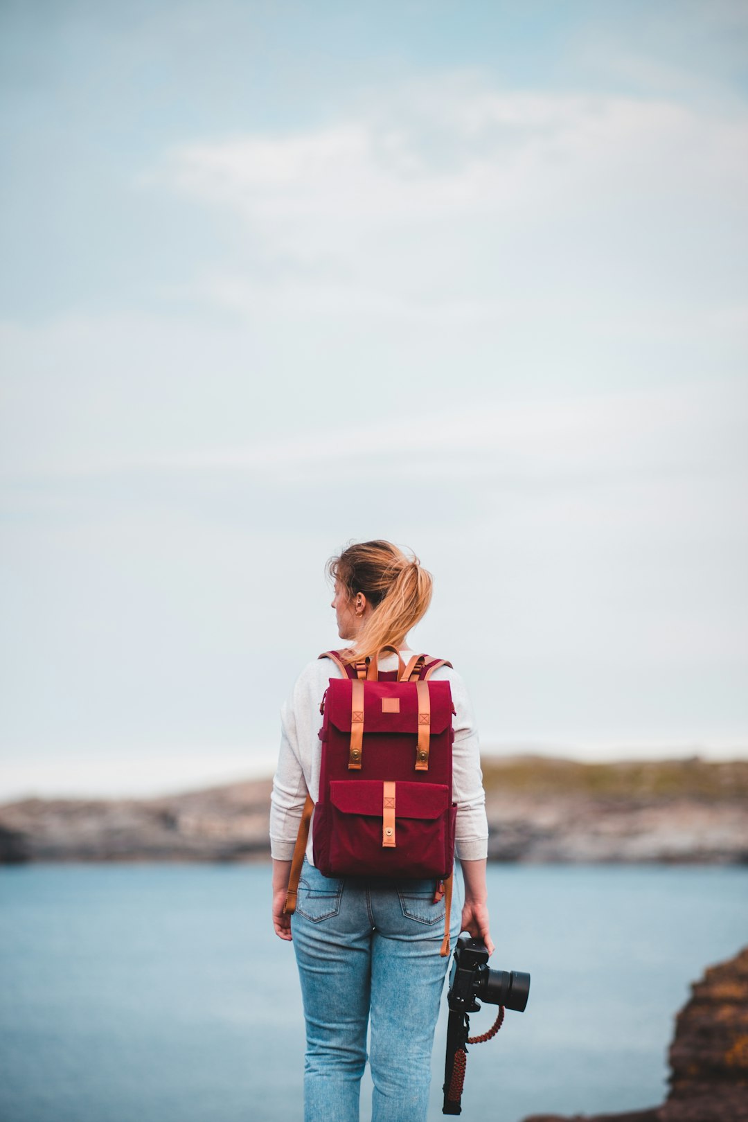 woman in white shirt and orange backpack standing near body of water during daytime