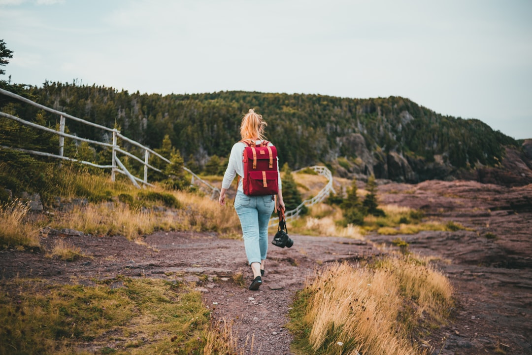 woman in red and white jacket walking on brown dirt road during daytime