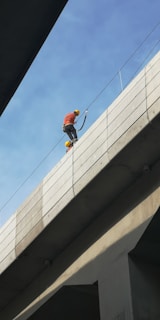 man in orange jacket and black pants climbing on gray metal pole during daytime