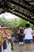 A vibrant farmers market bustling with smiling families and colorful produce under a sunny sky.