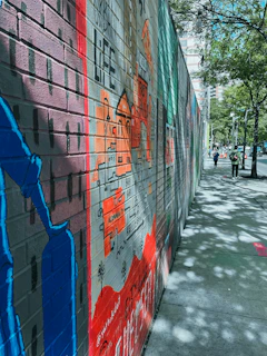 A colorful street artist painting a mural on a brick wall in the afternoon.