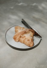 Close-up of a golden miso croissant resting on a rustic wooden board with a backdrop of olive-toned ceramics and soft natural light.