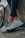 A pair of legs in dark leggings are leaning against a concrete surface next to a bicycle wheel. The person is wearing light-colored athletic shoes with intricate patterns and details, featuring shades of gray, blue, and red.