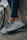 A pair of legs in dark leggings are leaning against a concrete surface next to a bicycle wheel. The person is wearing light-colored athletic shoes with intricate patterns and details, featuring shades of gray, blue, and red.