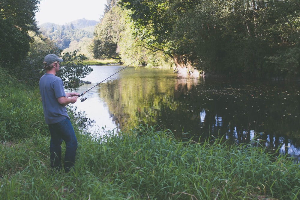 man in blue shirt fishing on lake during daytime