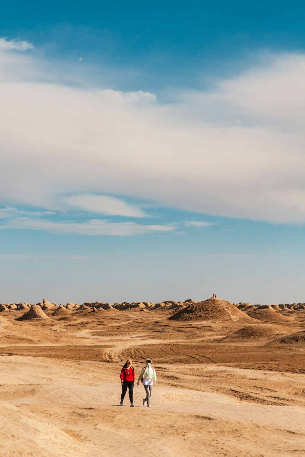 Persona con camisa blanca caminando sobre arena marrón bajo el cielo azul durante el día