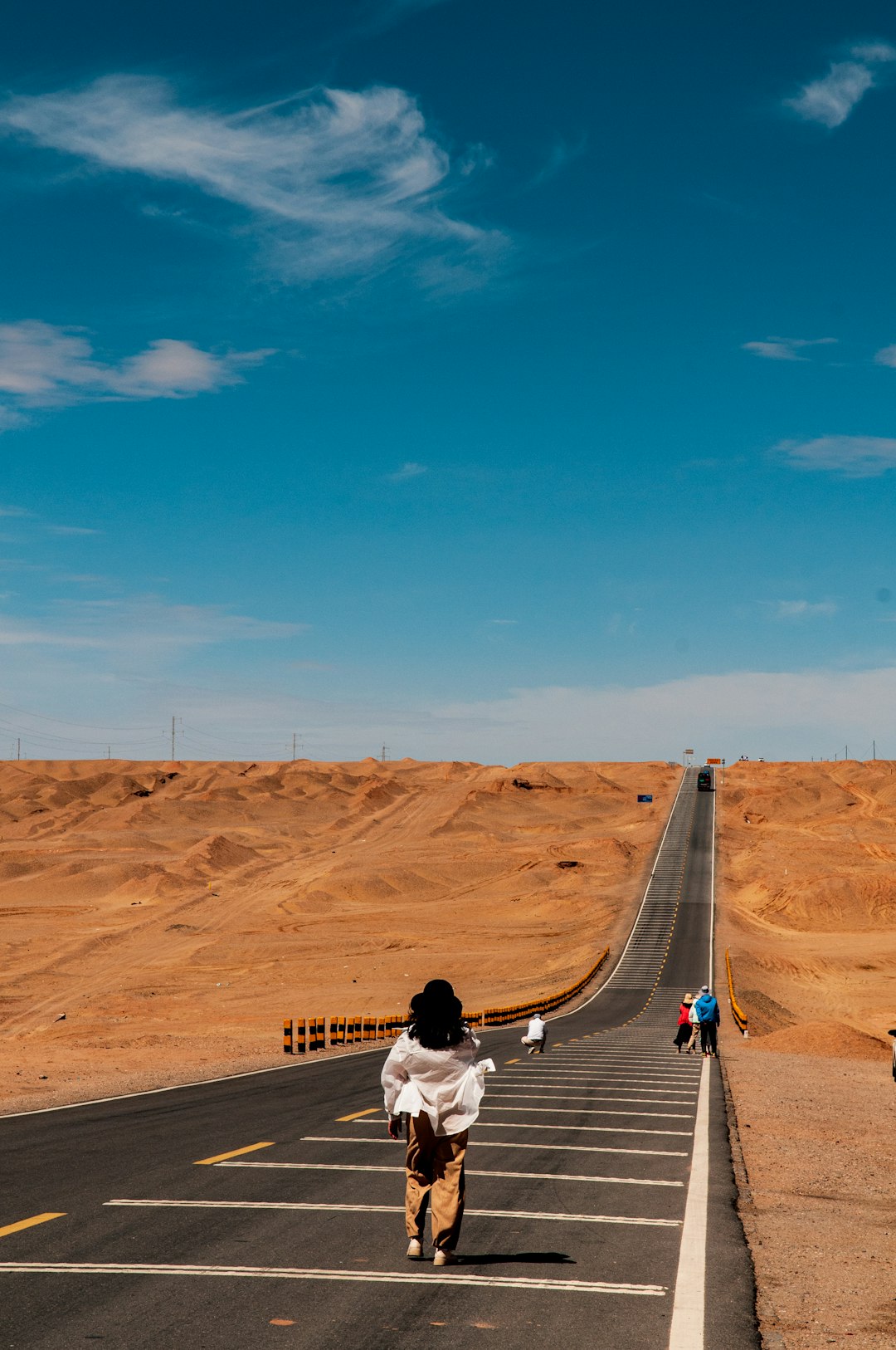 woman in white long sleeve shirt and blue denim jeans walking on gray asphalt road during