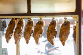 Several roasted ducks are hanging in a row inside a glass-fronted display case, likely in a food market or restaurant setting.
