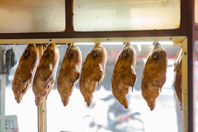 Several roasted ducks are hanging in a row inside a glass-fronted display case, likely in a food market or restaurant setting.