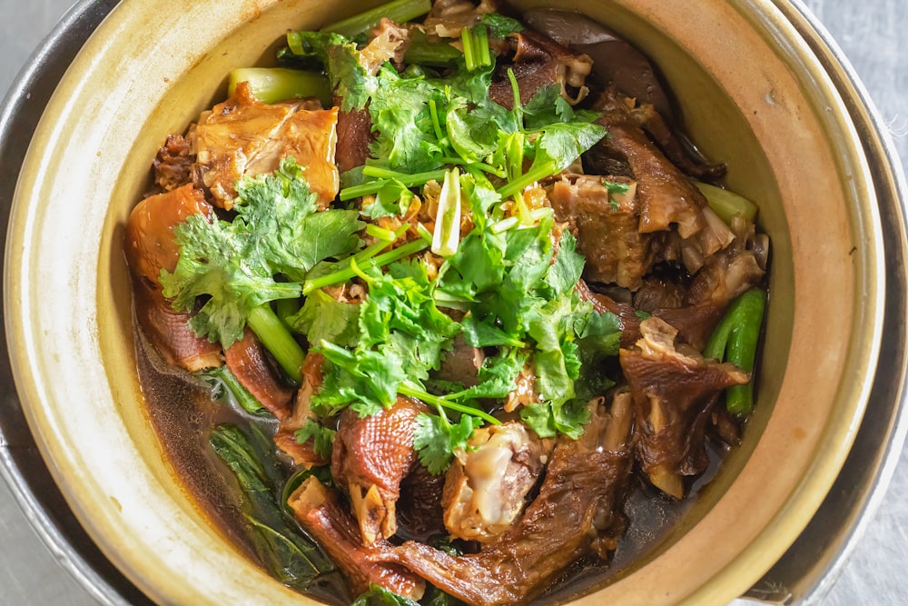 cooked meat with green vegetable in brown ceramic bowl