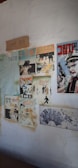 The image depicts a wall decorated with vintage comic book posters and a calendar from the year 1970. The posters feature various illustrated characters, predominantly in Korean text, and include elements such as a man holding a gun, a woman, and other stylized figures. There is also a piece of paper with handwritten text.