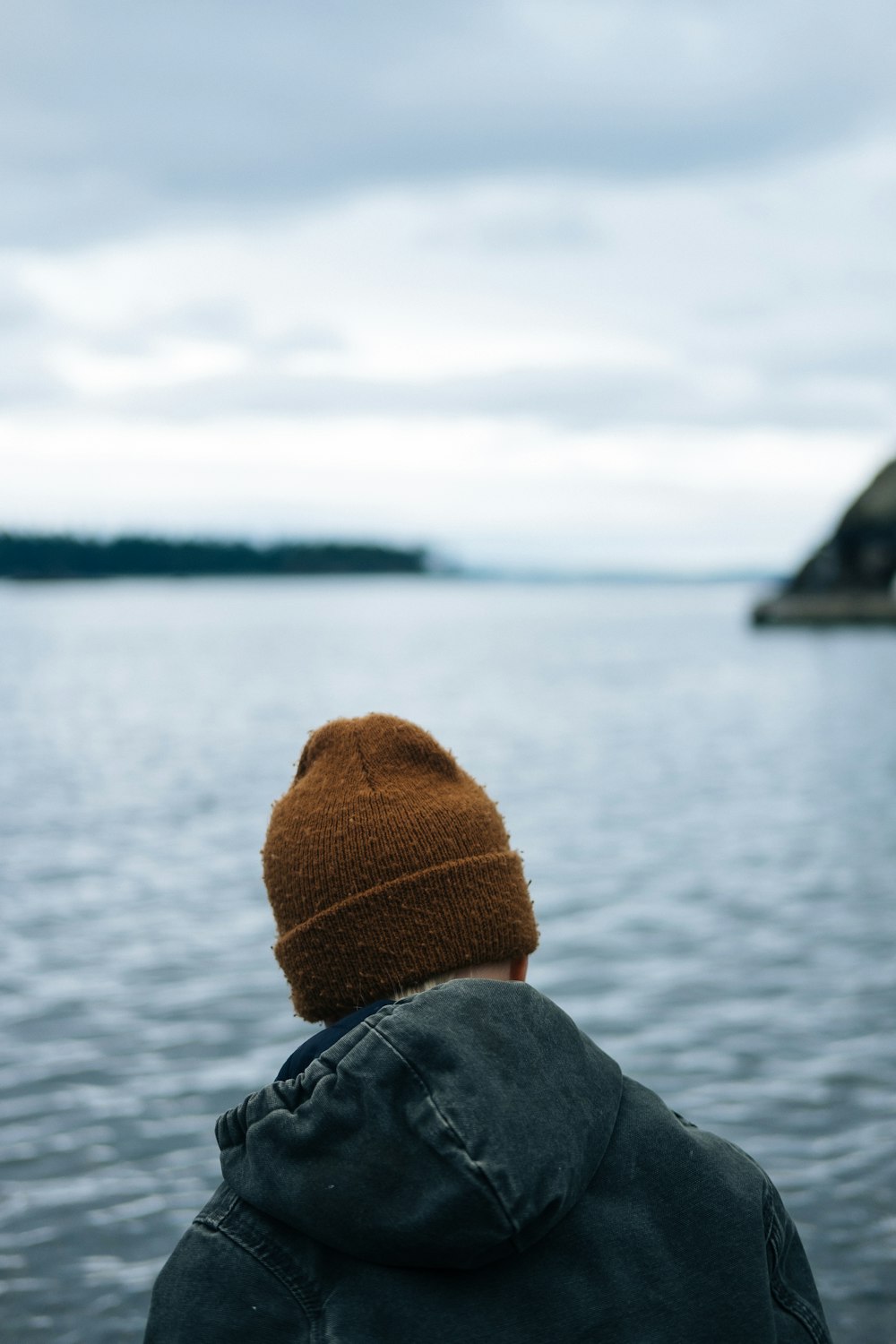 person in black jacket wearing brown knit cap looking at sea during daytime