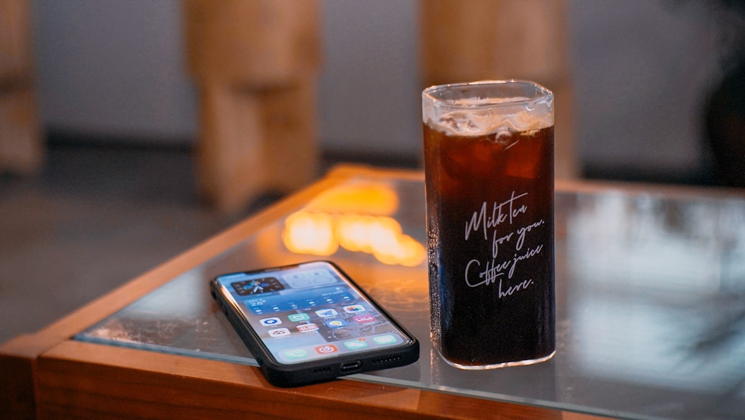 black iphone 5 beside clear drinking glass on brown wooden table