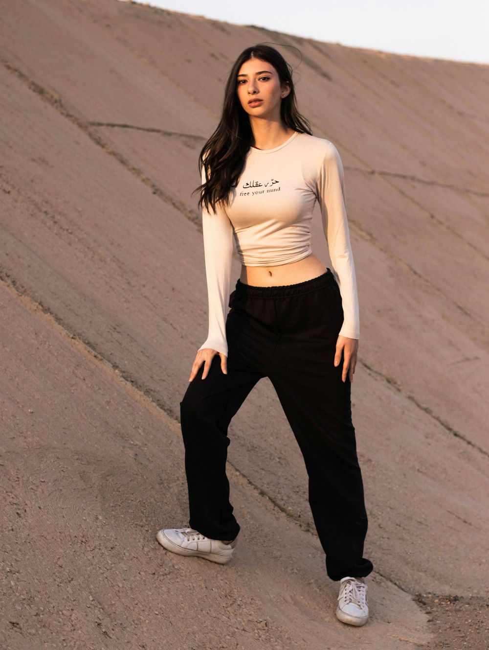 woman in white long sleeve shirt and black pants standing on gray asphalt road during daytime