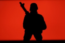 A silhouette of a soldier holding a weapon against a vibrant red background. The figure is in a standing position, creating a strong and dramatic contrast with the backdrop.