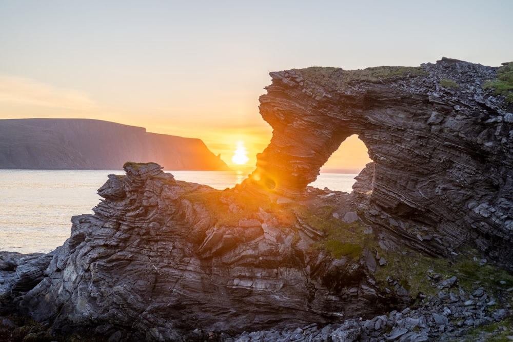brown rock formation near body of water during sunset