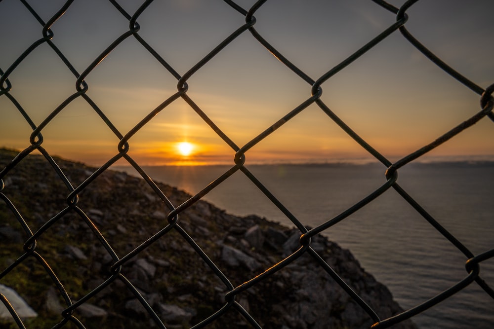 grey metal fence near body of water during sunset