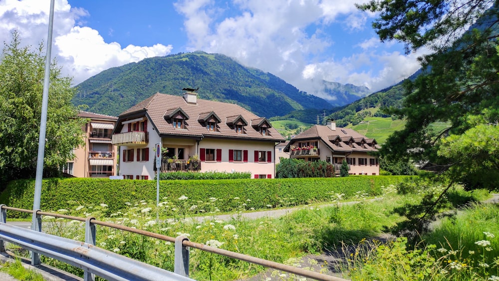 Braunes und weißes Haus in der Nähe von grünem Grasfeld und Berg unter blauem Himmel tagsüber