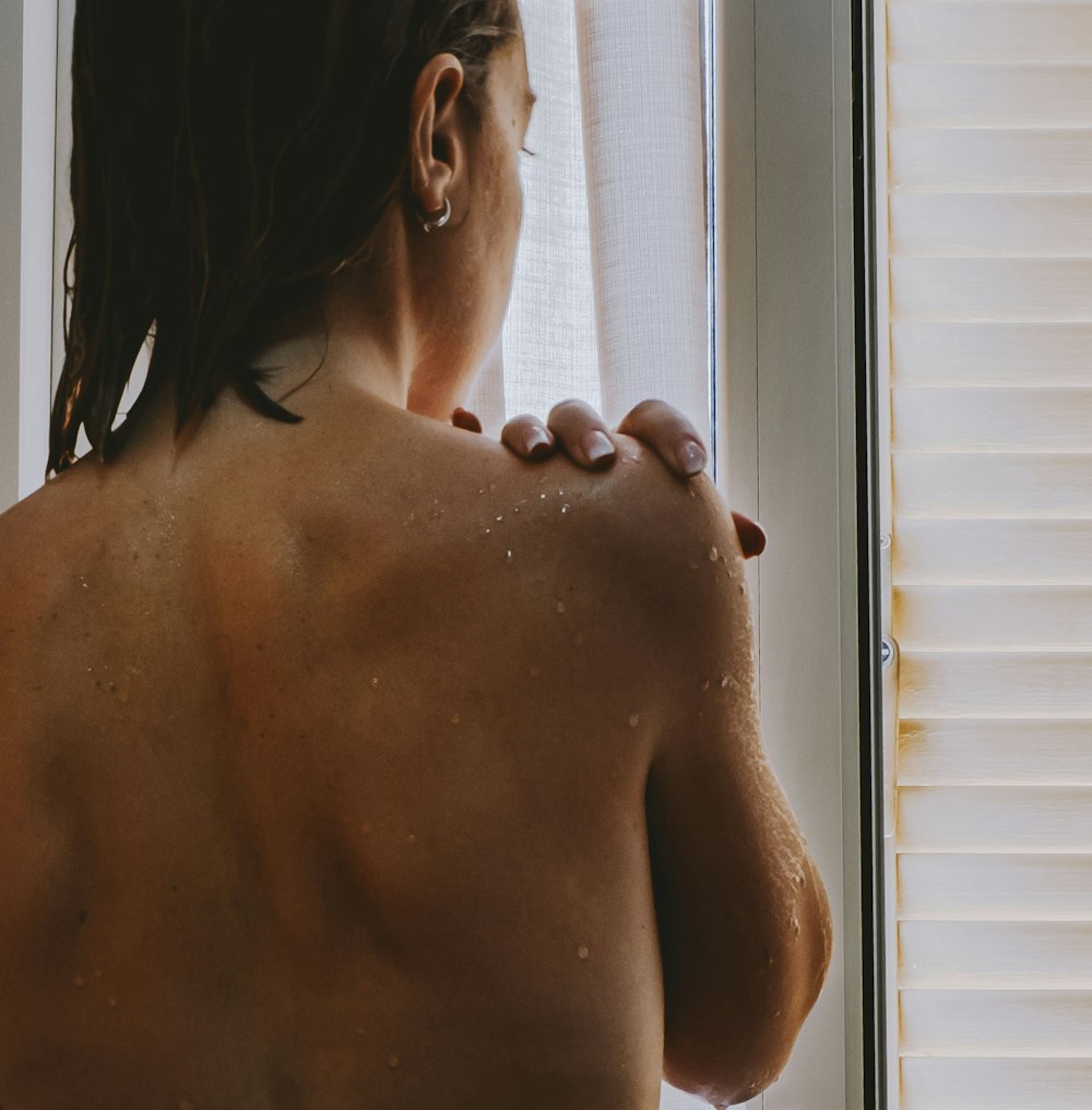 topless woman standing near window blinds
