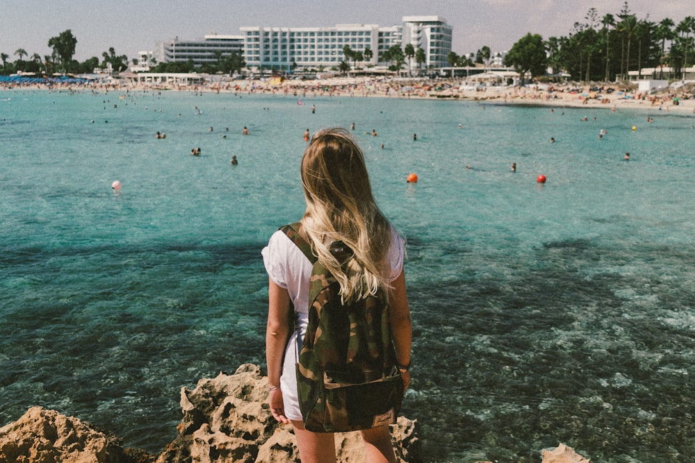 femme en chemise blanche et short marron debout sur une formation rocheuse près d’un plan d’eau pendant