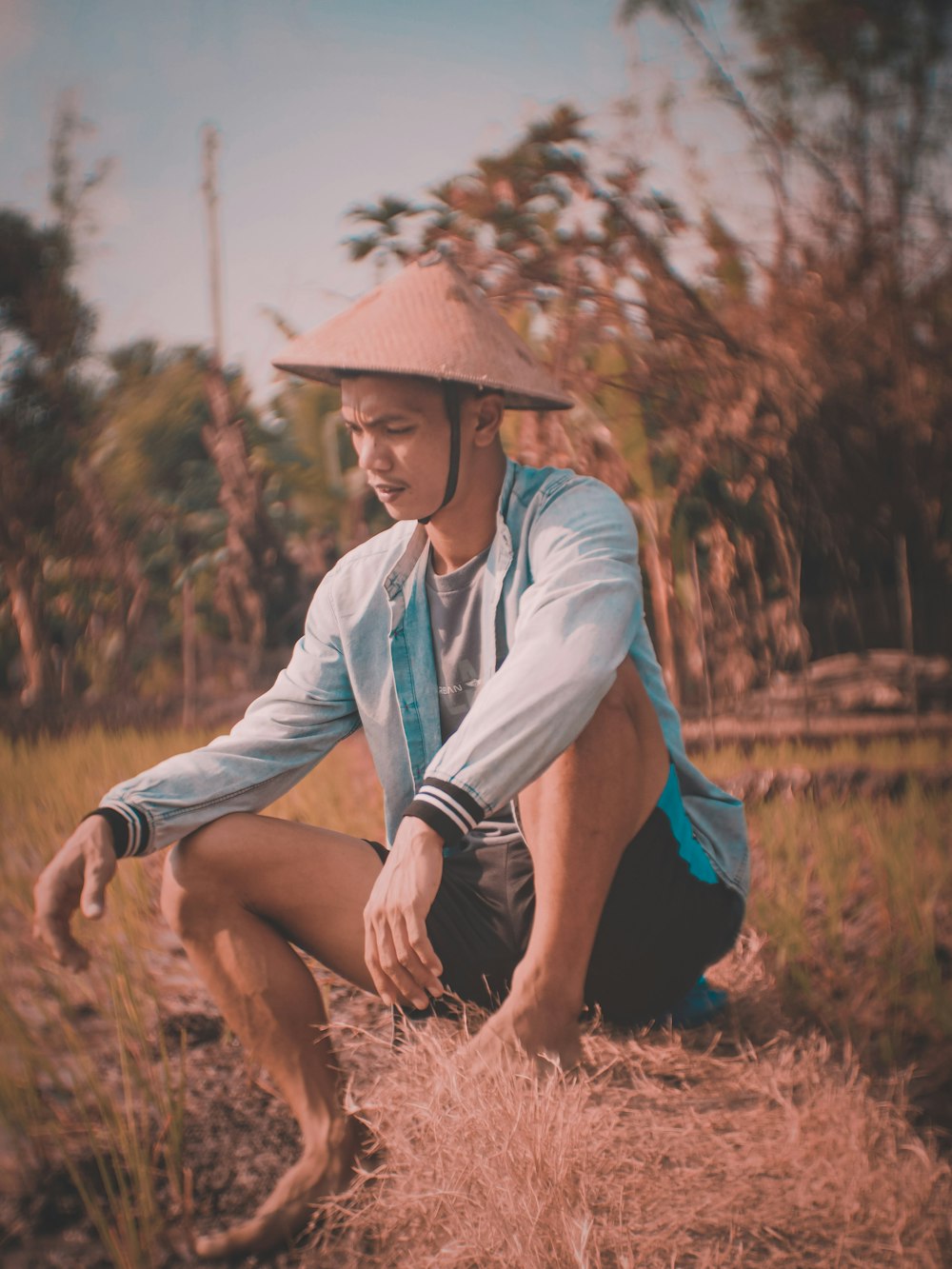 woman in blue long sleeve shirt and brown hat sitting on brown grass field during daytime