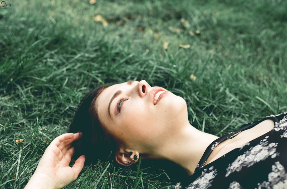 woman in black and white floral shirt lying on green grass field