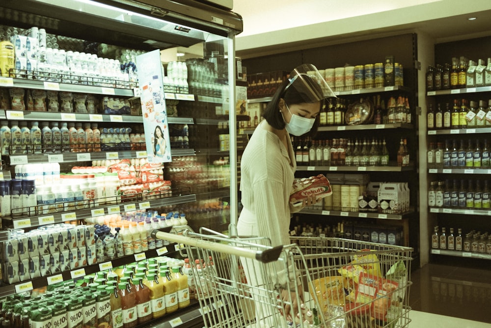 Femme en chemise blanche à manches longues et hijab blanc debout devant l’étagère de l’épicerie