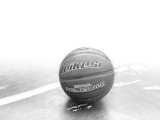 A basketball with the branding 'Leikesi Official Premier Pro' is placed on a textured surface with a white line running diagonally. The image has a monochromatic tone with focus on the ball, creating a dramatic visual contrast.