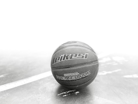 A basketball with the branding 'Leikesi Official Premier Pro' is placed on a textured surface with a white line running diagonally. The image has a monochromatic tone with focus on the ball, creating a dramatic visual contrast.