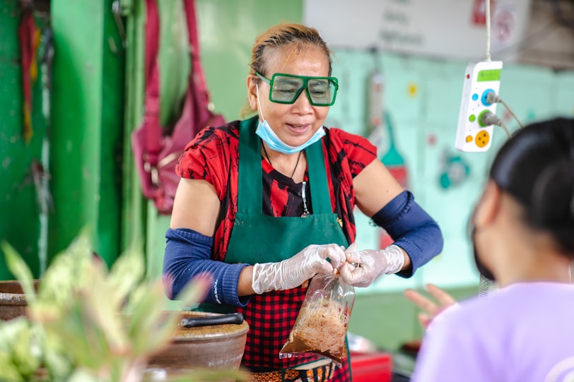 Where to stay in Bangkok: Sukhumvit woman in red and black vest wearing green goggles selling food