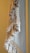 A close-up view of a textile with intricate macramé patterns and numerous fringed tassels in neutral tones. The woven design features a combination of tightly wrapped and loosely knotted textures, creating a sense of handcrafted elegance.