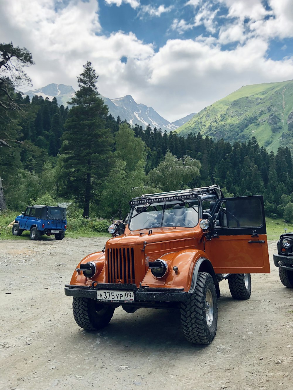 orange jeep wrangler on dirt road near green trees during daytime