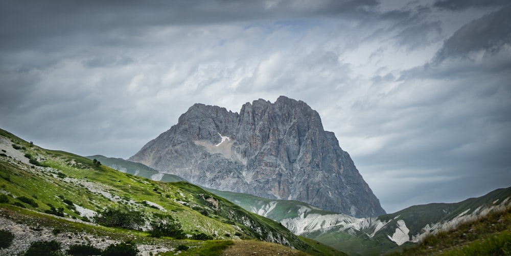 green grass field near gray and white mountain under white clouds during daytime