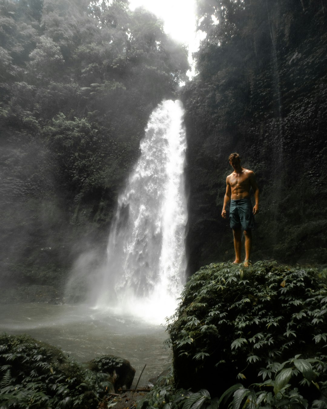 woman in blue shorts standing on rock near waterfalls during daytime