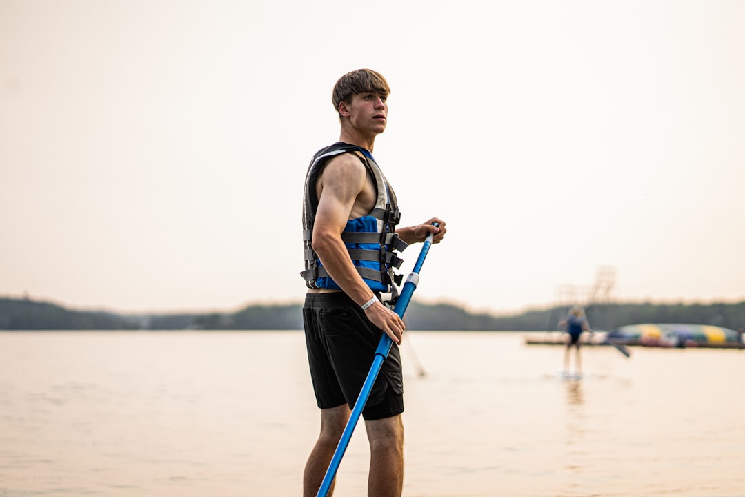 man in black tank top and blue shorts holding brown acoustic guitar standing on beach during