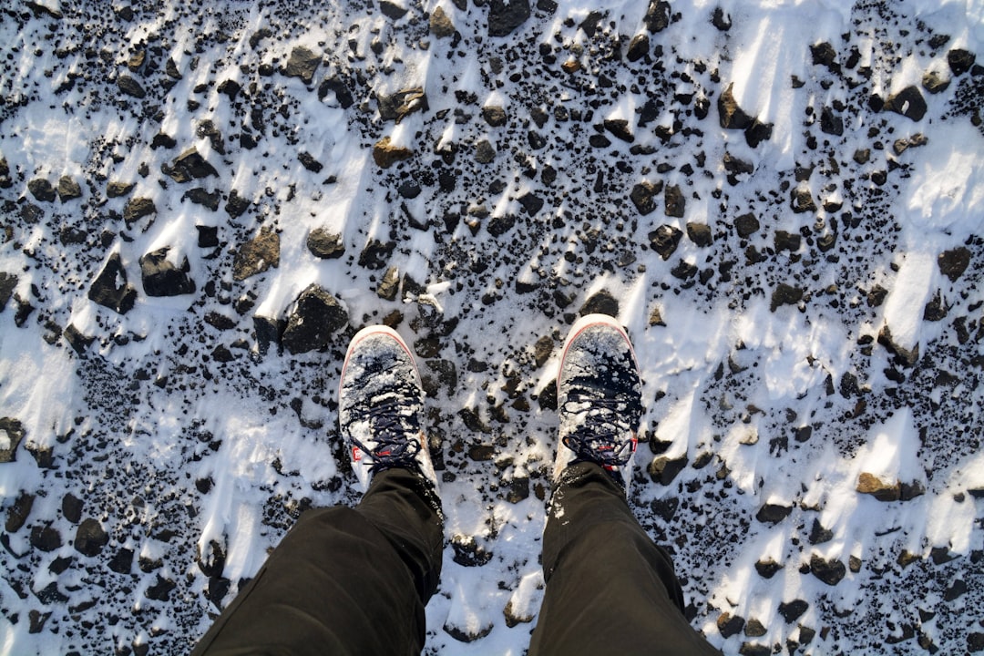 person in black pants and brown hiking shoes standing on snow covered ground during daytime