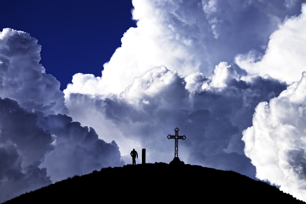 silhouette of cross on top of hill under white clouds and blue sky during daytime