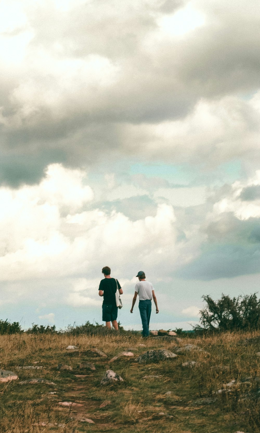 homme et femme marchant sur un champ d’herbe brune sous des nuages blancs pendant la journée