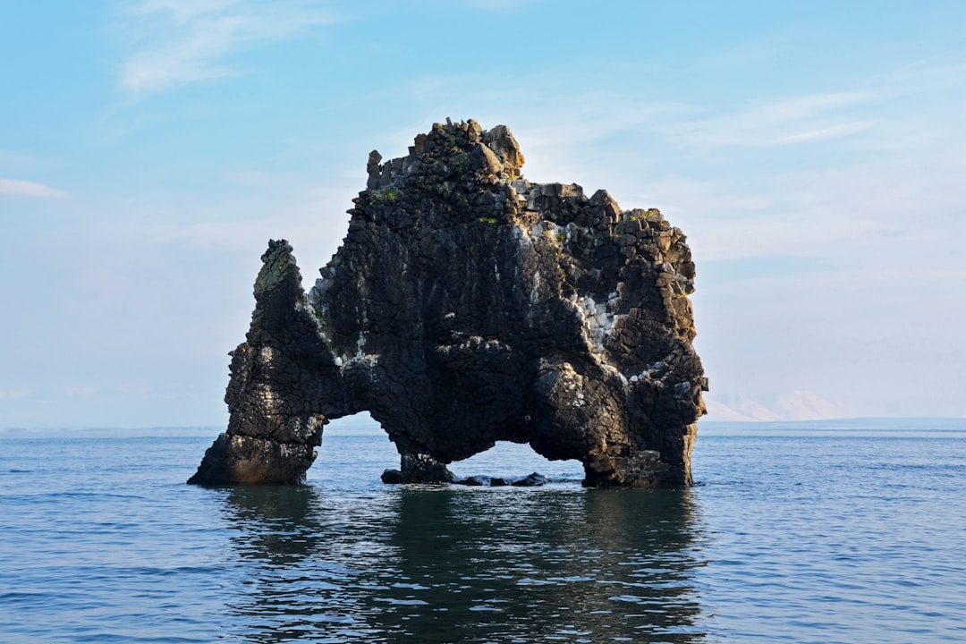 brown and green rock formation on sea under blue sky during daytime