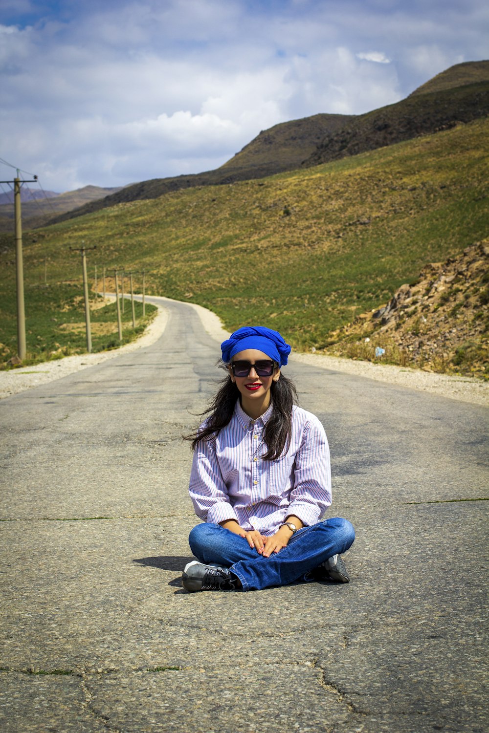 woman in blue denim jeans sitting on gray concrete road during daytime