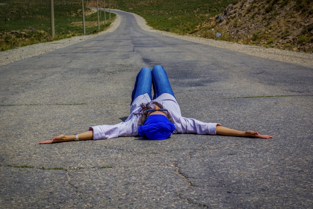 person in blue denim jeans and white sneakers lying on gray concrete road during daytime